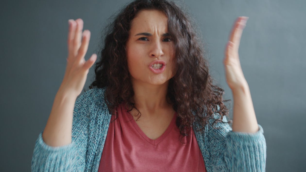woman in blue sweater and red shirt with hands raised next to her face