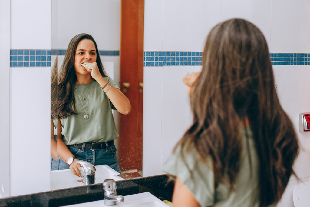 Young Woman Brushing Teeth in Bathroom Mirror
