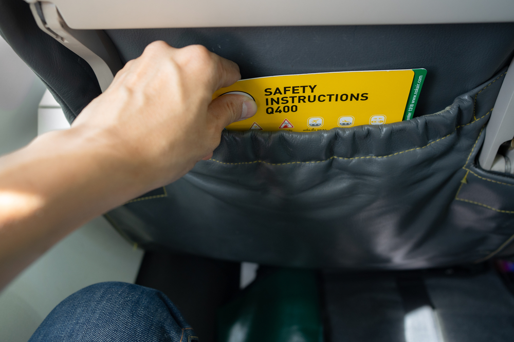 Close-up of Asian male's hand picking aircraft safety card or an emergency information instruction manual from the airplane seat pocket in front of him. safety card to be at every seatback on airplaneThe hidden mess on your flight is right in front of you.
