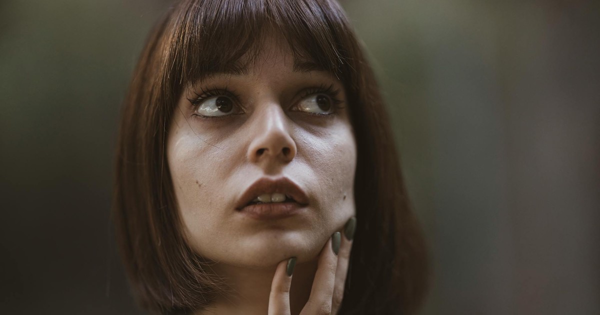 Close-up portrait of a brunette woman looking pensive with dramatic lighting and a soft background.