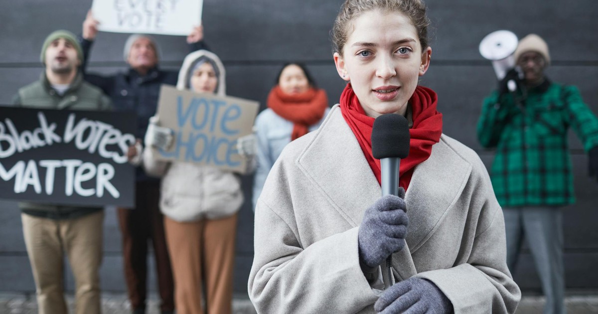 Female journalist reporting live from a protest with diverse activists and signs advocating voting rights.