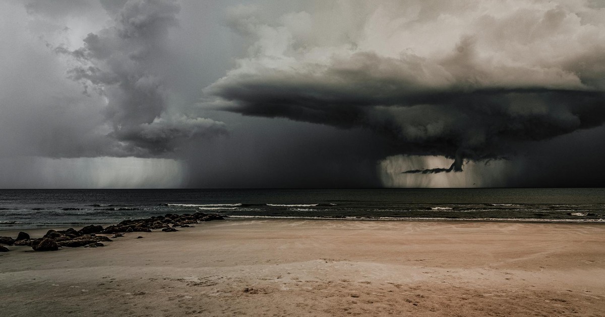 Dark storm clouds gather menacingly over a deserted beach by the ocean.