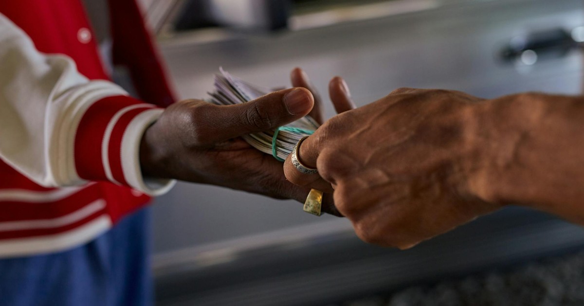 A detailed shot of two hands exchanging a bundle of cash outside by a car.