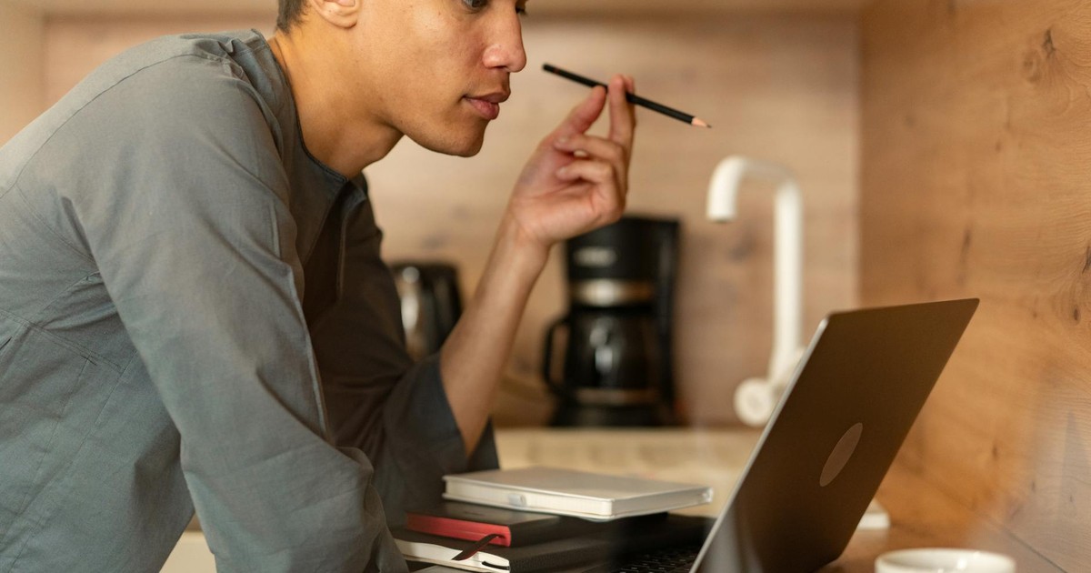 Man studying attentively on laptop with notebooks and coffee in a cozy kitchen workspace.