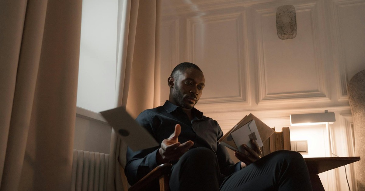 Man with a mustache reading a letter in a dimly lit home interior, creating a serene atmosphere.