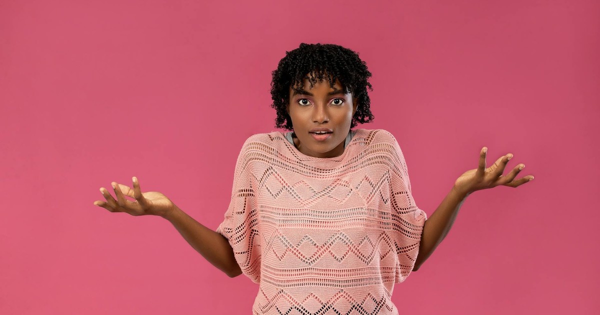 Young woman expressing confusion or uncertainty with a puzzled look on a pink background.