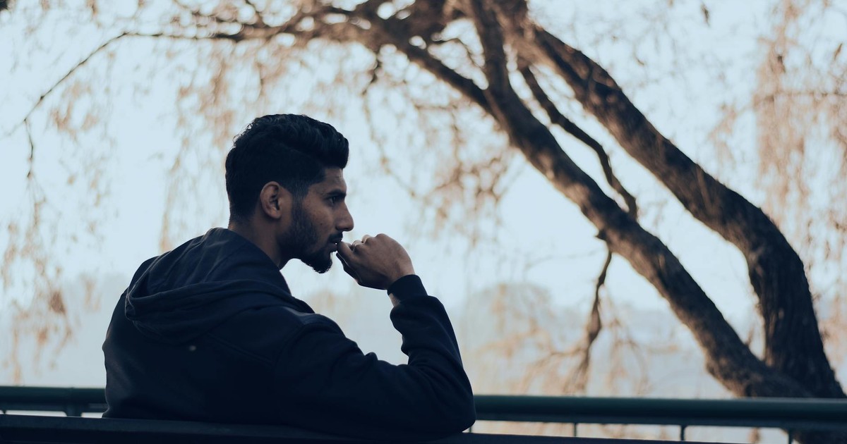 Man in deep thought sitting on a bench in a serene autumn park setting.