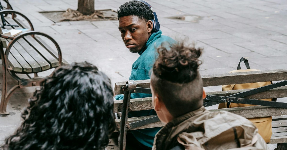 Back view of anonymous classmates sitting behind black friend and gossiping on schoolyard