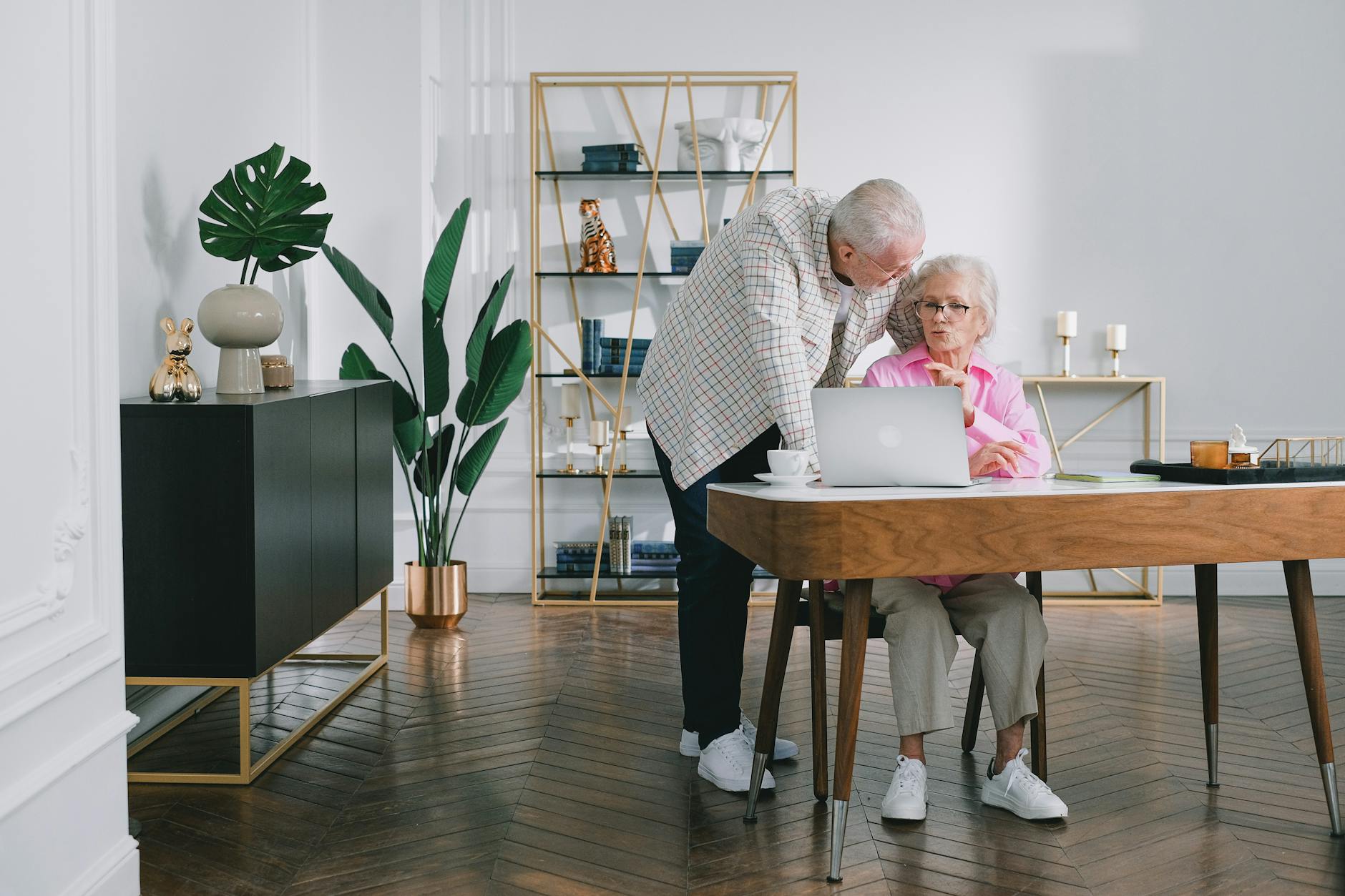 Senior couple using a laptop while discussing something in their modern living room.