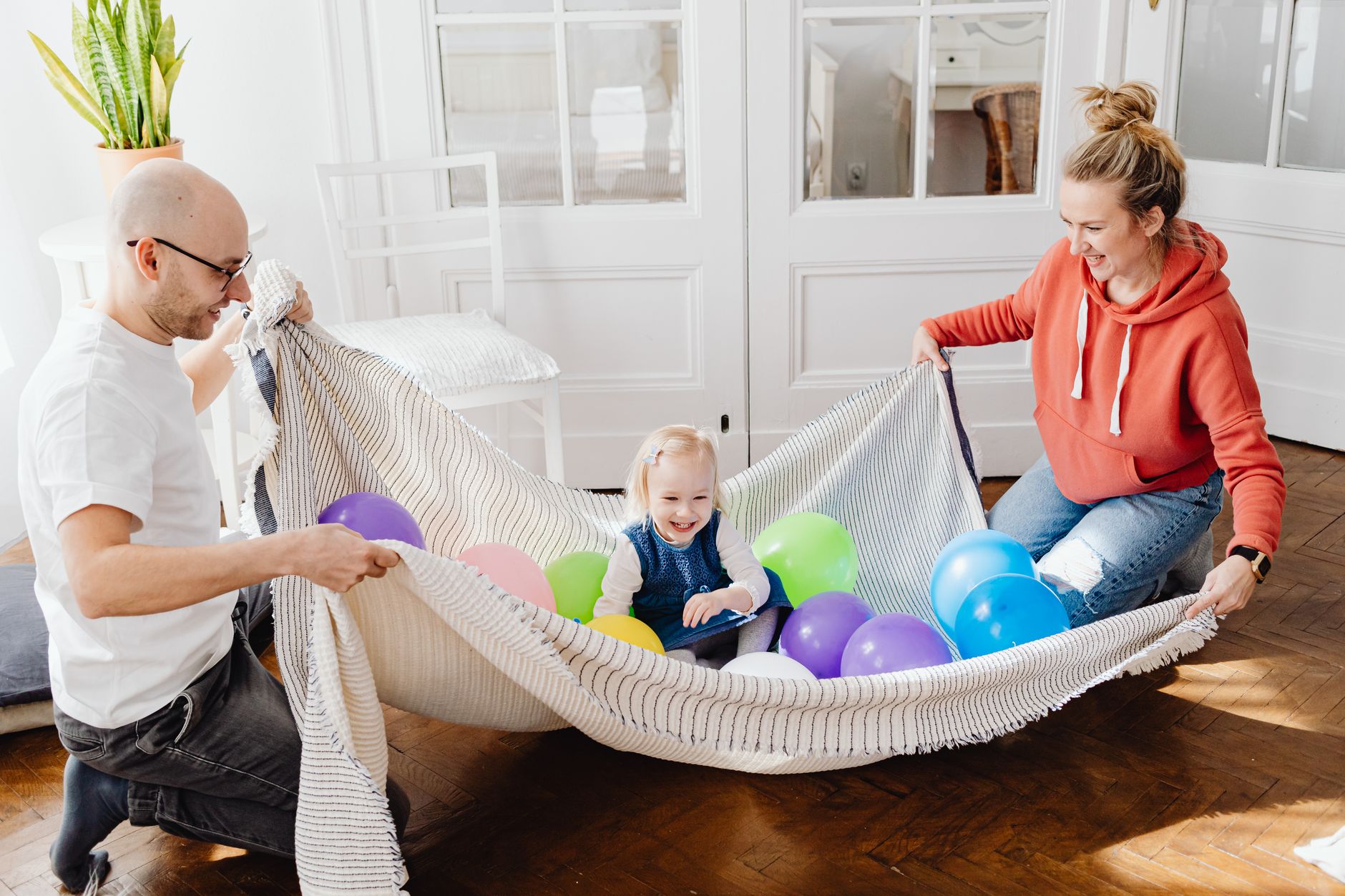 Joyful parents playing with their child using colorful balloons indoors.