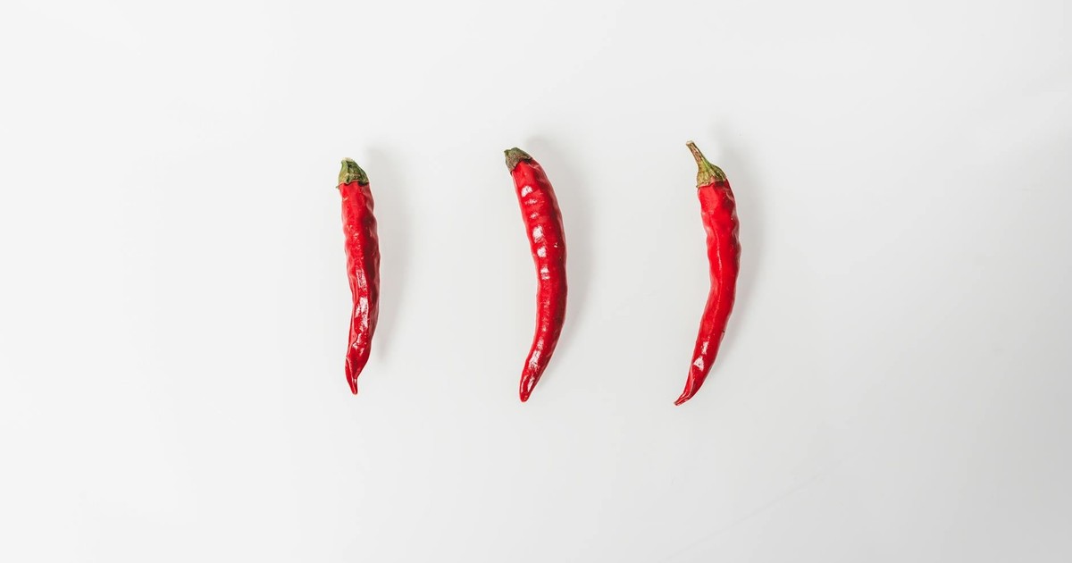 Three red chilies arranged on a white background in a minimalist style.