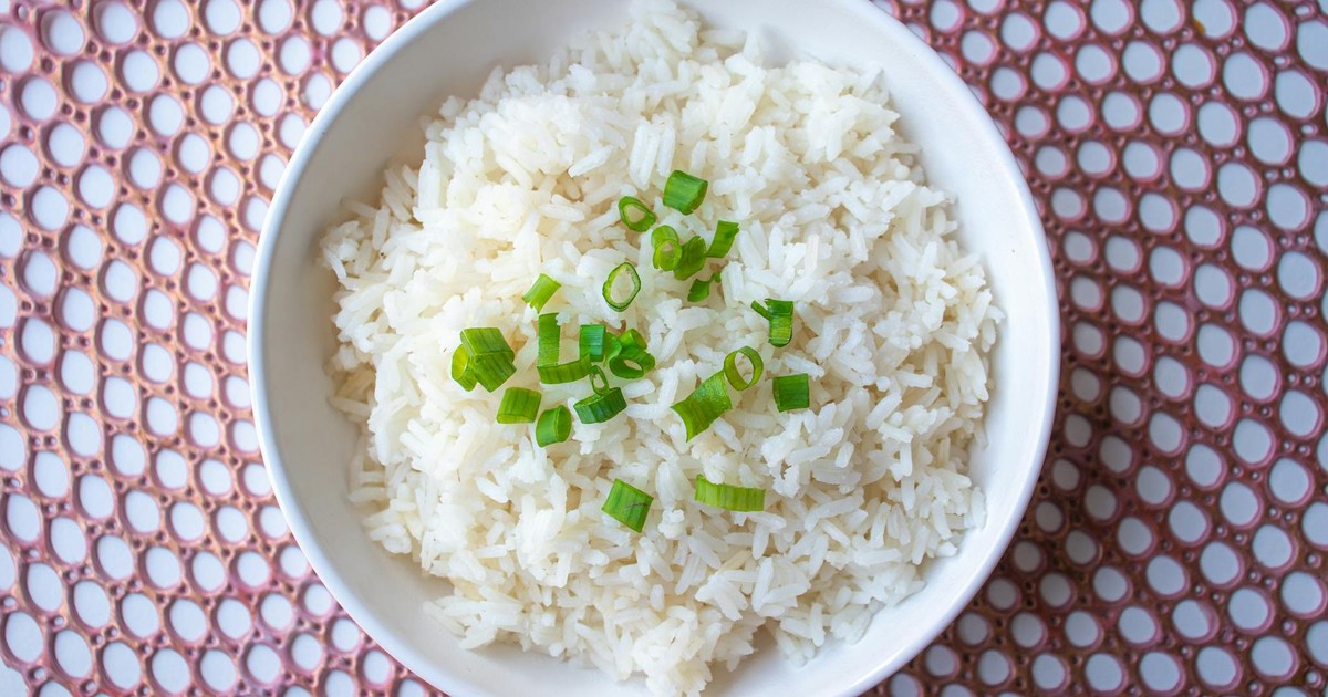 A bowl of cooked white rice garnished with green onions, perfect for culinary presentations.