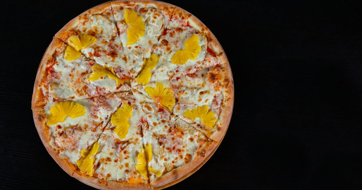 A mouthwatering Hawaiian pizza topped with cheese and pineapple on a dark background.
