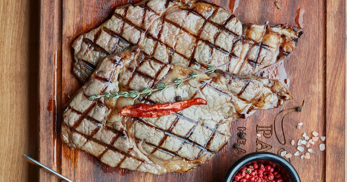 Juicy grilled steaks garnished with herbs on a wooden board with peppercorns and vegetables.