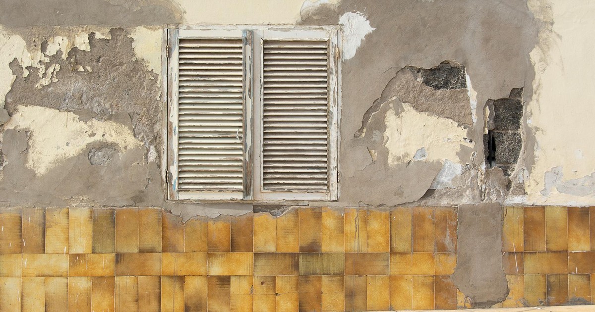 Close-up of an old wall with weathered shutters, peeling paint, and tiled base.