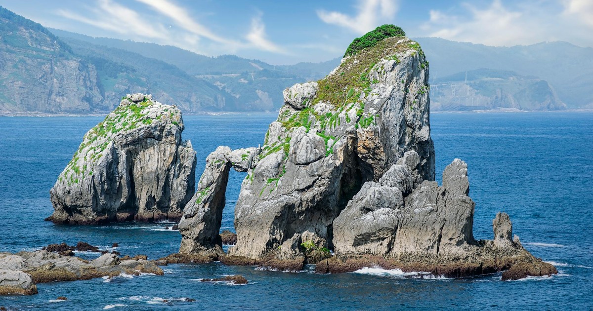 Stunning coastal rock formations with natural arches and lush greenery by the ocean.