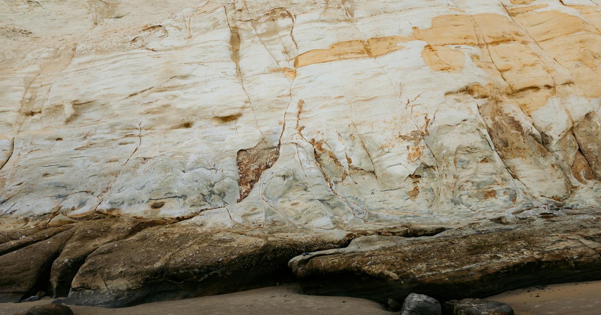 Detailed view of a weathered coastal rock formation with sandy foreground, showcasing natural erosion.