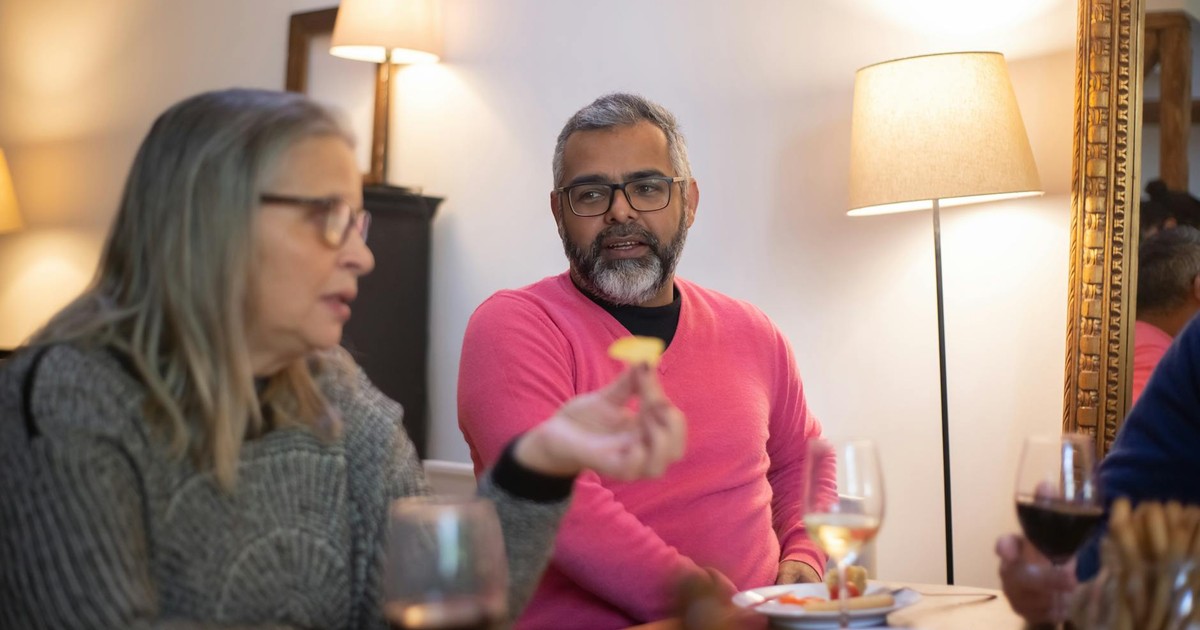 Two senior adults enjoying a casual conversation over drinks in a cozy indoor setting.
