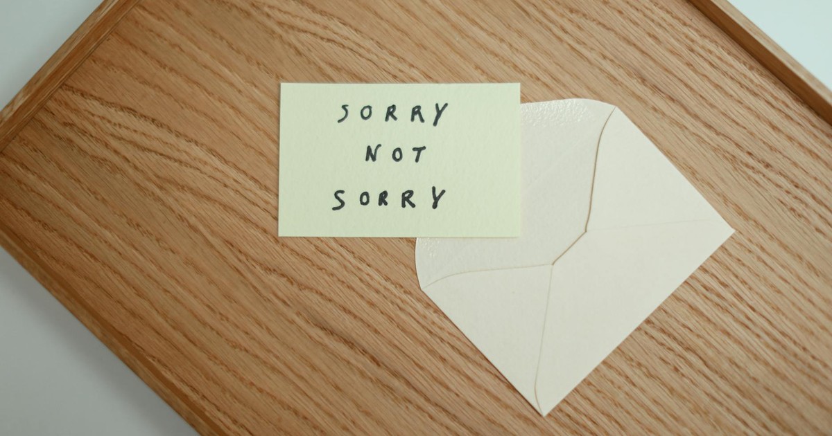 A flat lay of a 'Sorry Not Sorry' card with an envelope on a wooden surface.