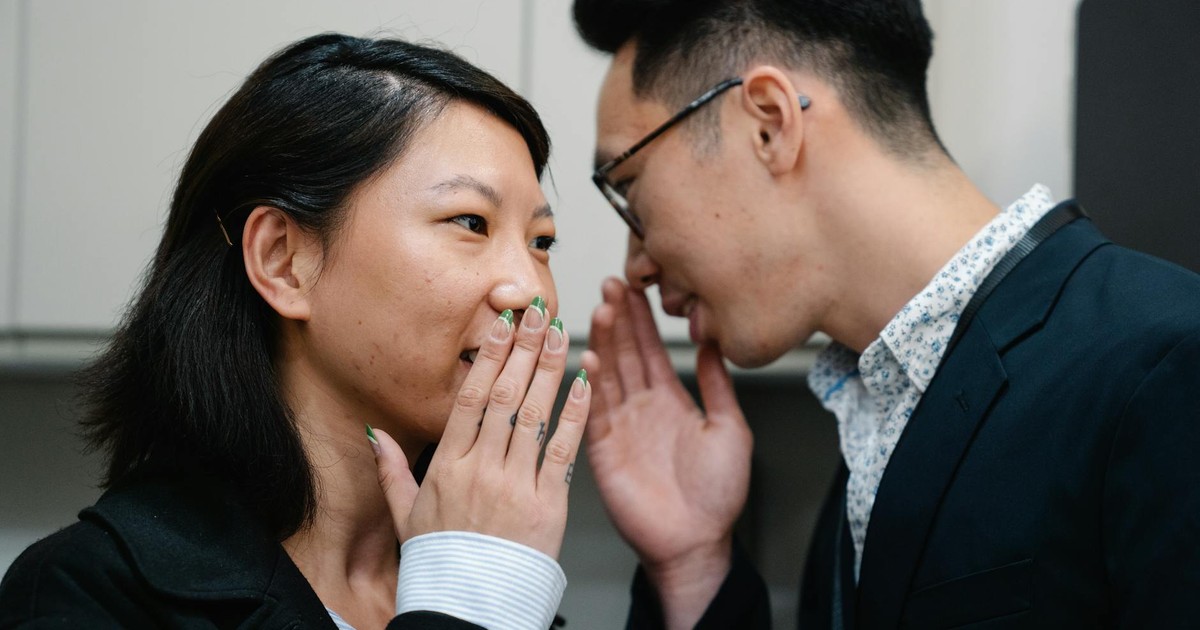Close-up of an Asian man and woman whispering secrets while indoors.