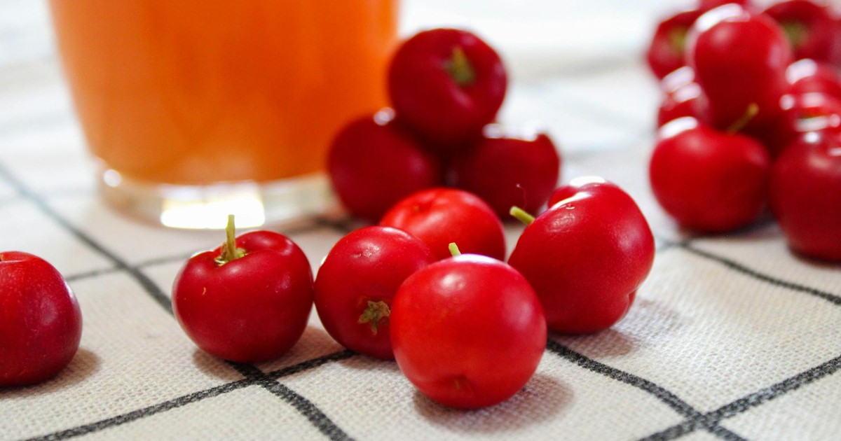 A vibrant image of acerola cherries and juice on a plaid tablecloth, showcasing natural refreshment.