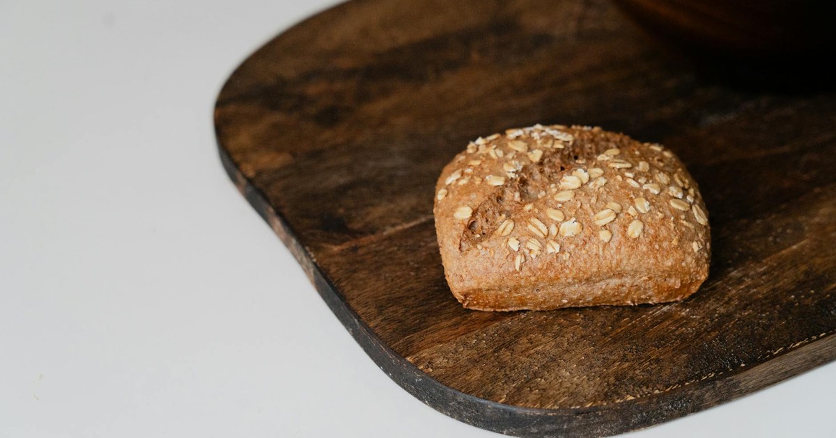 A freshly baked whole wheat bread roll with oats resting on a rustic wooden board.