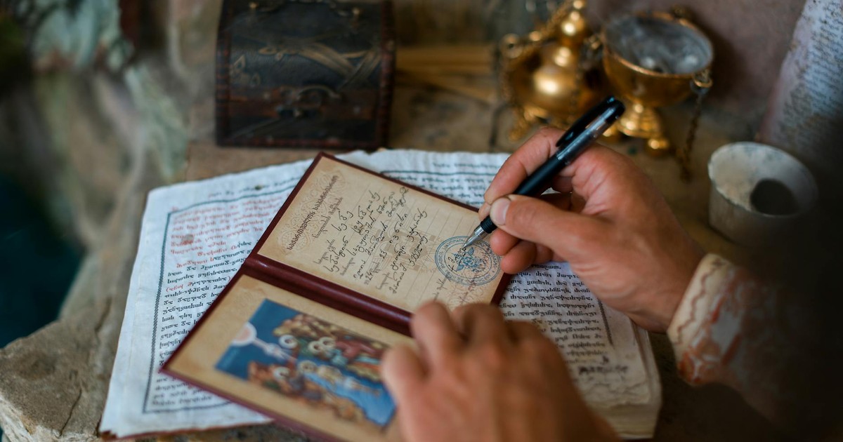 A person writes in an antique diary, surrounded by ancient artifacts and sacred texts.