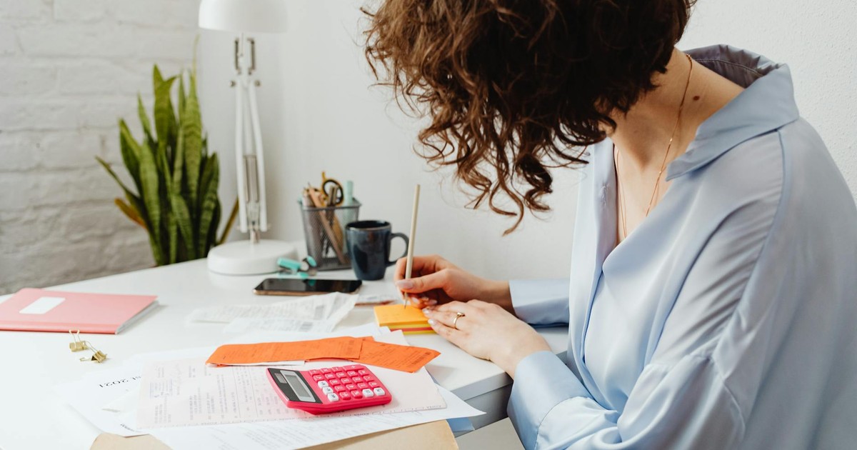 Woman writing with calculator on desk, managing finances indoors.