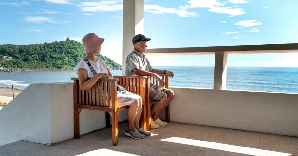 Senior couple sitting on balcony chairs, enjoying a relaxing ocean view in summer.