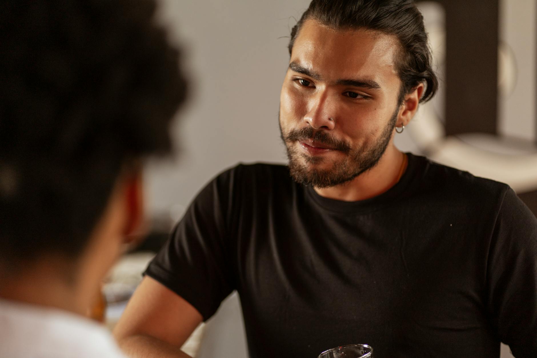 A bearded man attentively engaged in a conversation indoors, wearing a black shirt.