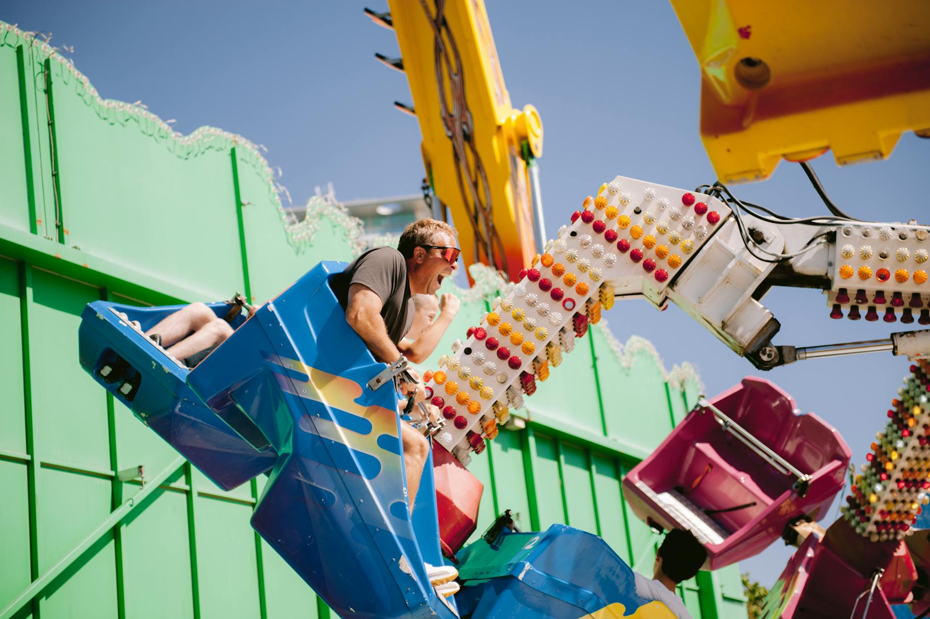 A vibrant scene of adults enjoying a thrilling amusement park ride under clear blue skies.