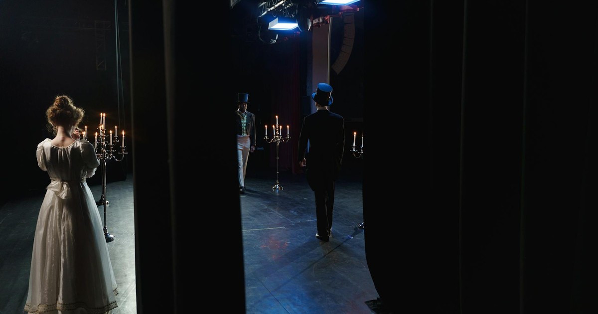 A captivating backstage view of actors in vintage costumes performing on a dimly lit theater stage.