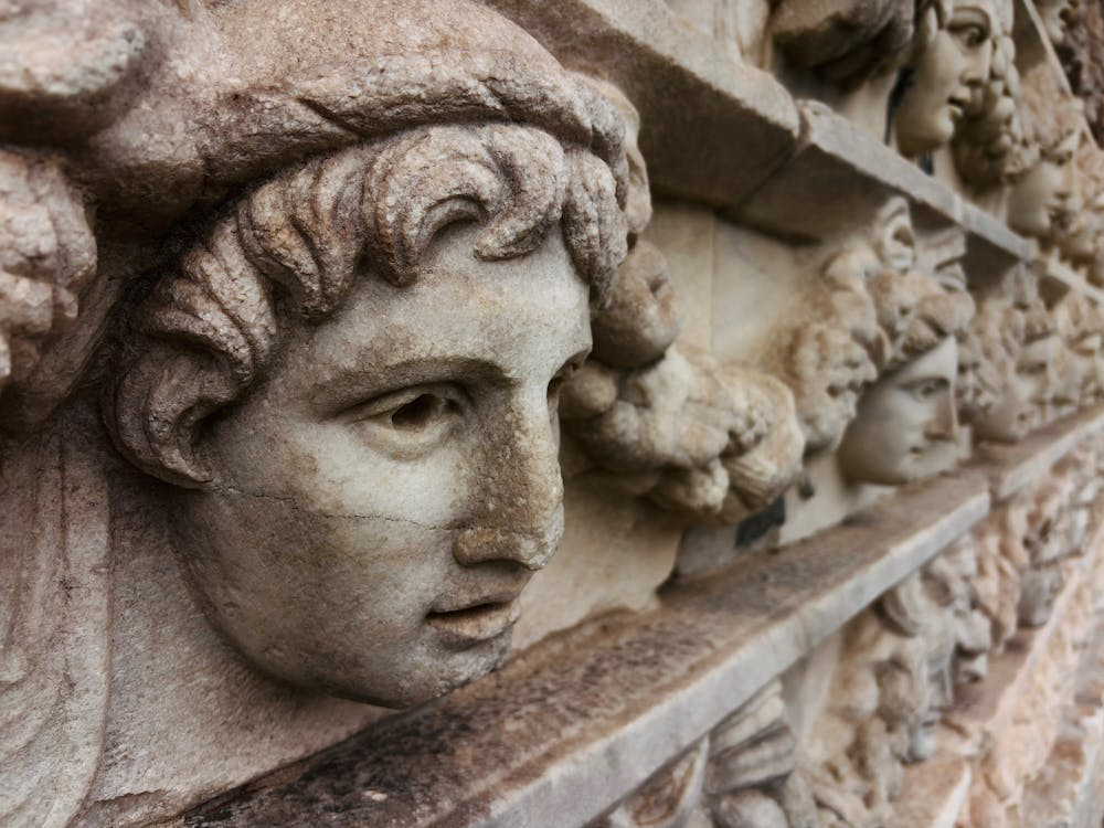 Close-up of ancient stone relief sculpture featuring detailed Greek faces