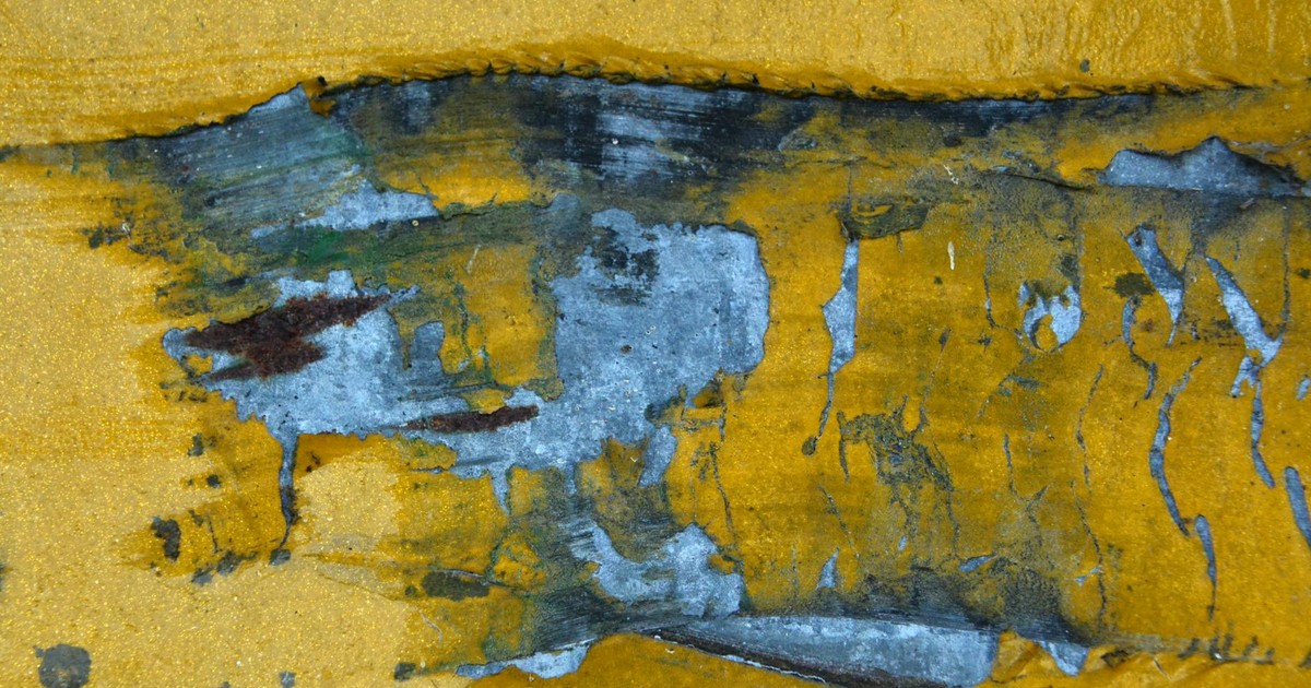 A detailed close-up of a weathered and peeling paint texture on a yellow concrete surface.