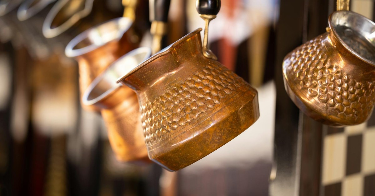 Close-up of traditional copper coffee pots hanging on a display rack, reflecting warm tones.