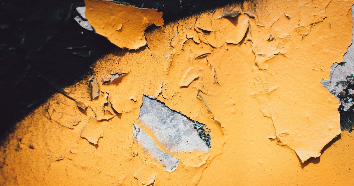 A detailed close-up of peeling yellow paint on a textured wall with visible decay.