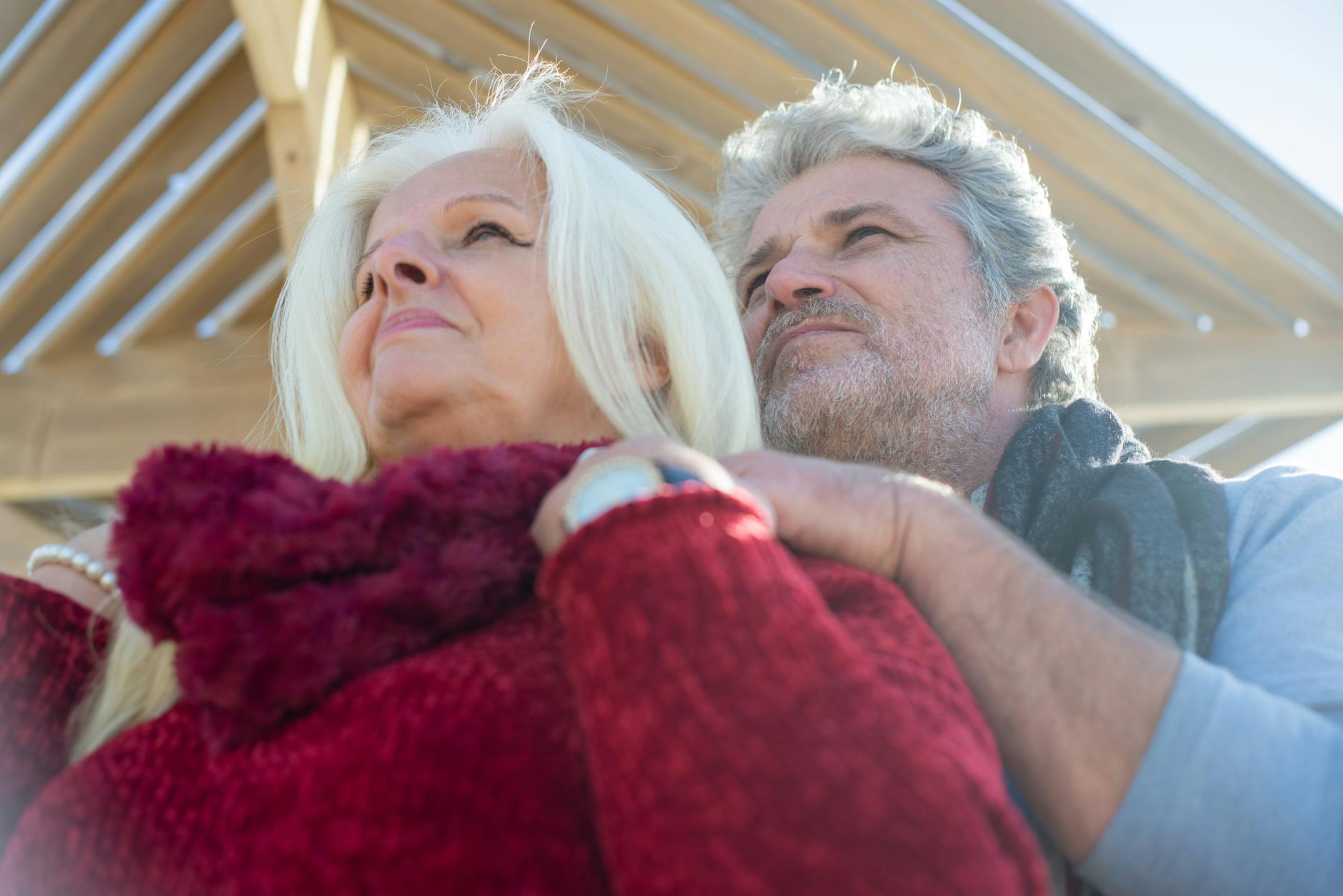 Loving senior couple embracing outdoors, under wooden structure in sunny Portugal.