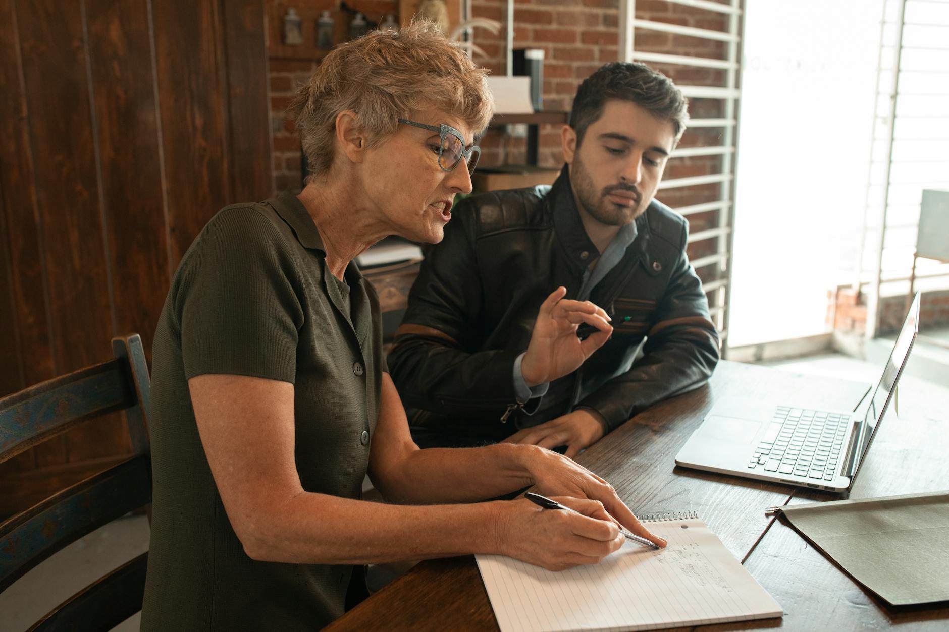 Senior woman guiding adult man during an indoor mentorship session with a laptop.