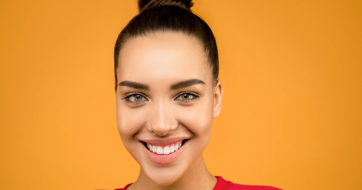 Portrait of a young woman smiling with elegant hairdo and bright background.