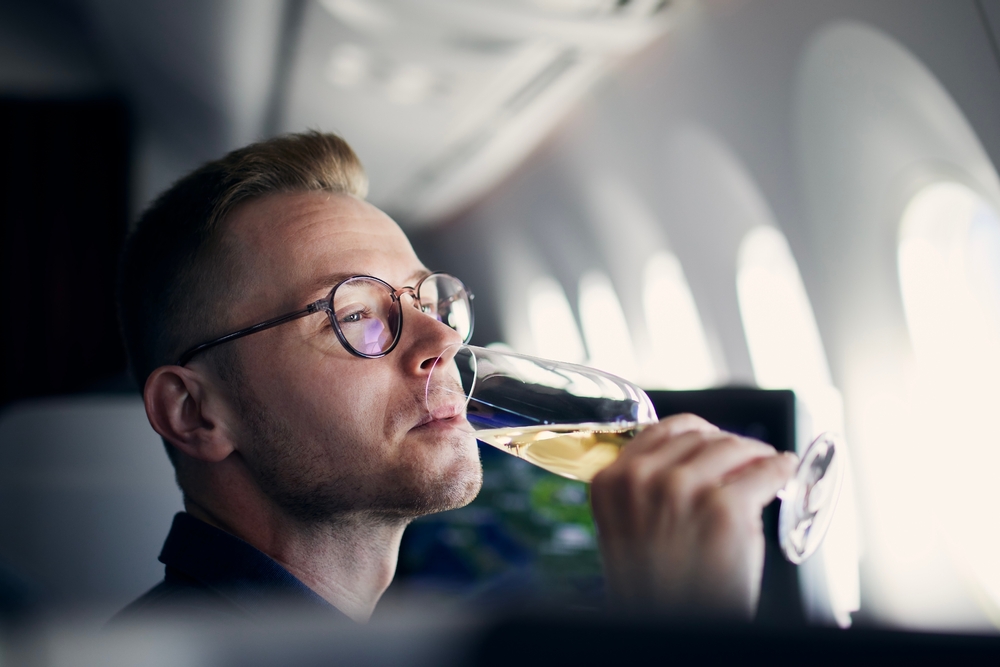 Business travel by airplane. Man looking through window and drinking champagne during flight.
