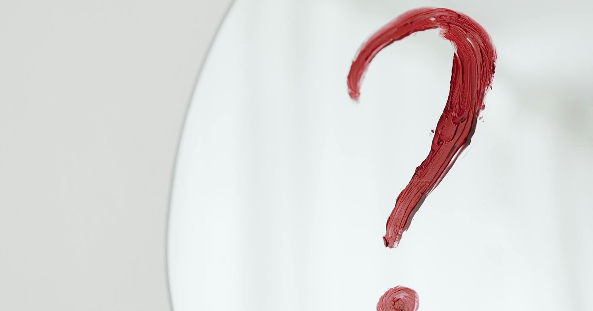 Close-up of a red question mark painted on a mirror with a white background.