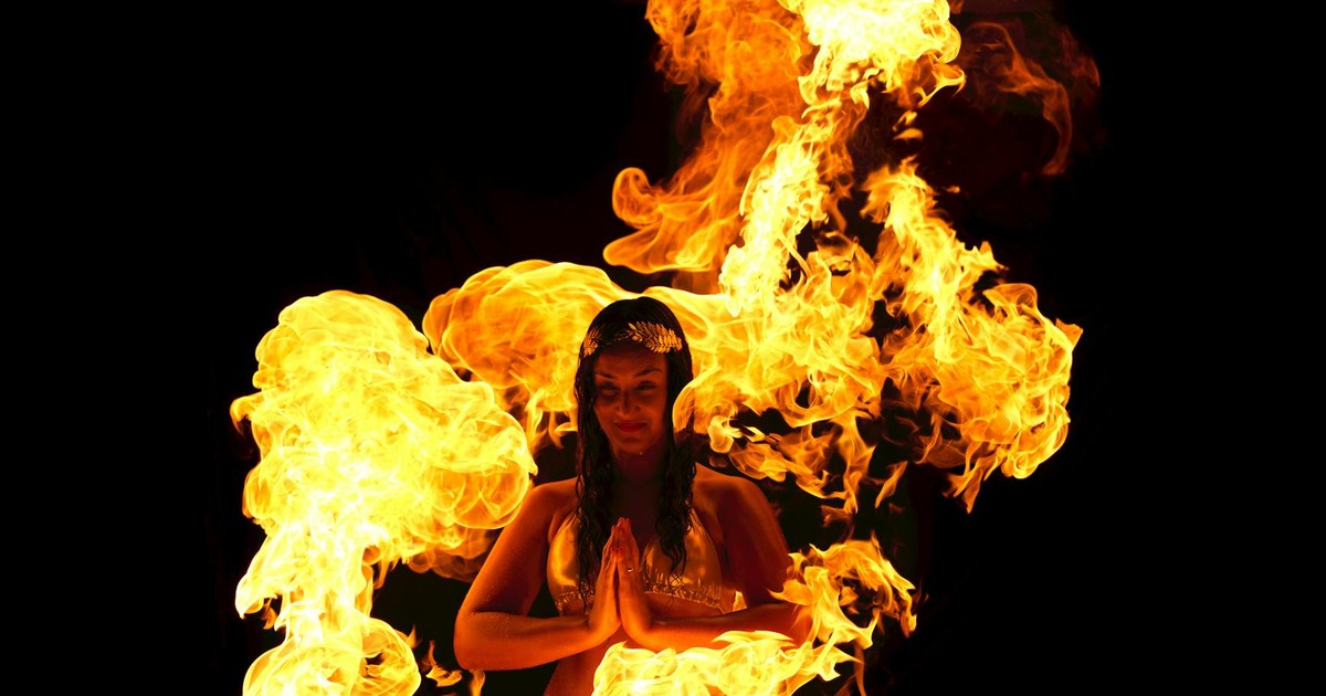 A woman performs a mesmerizing fire dance with surrounding flames on a dark background.
