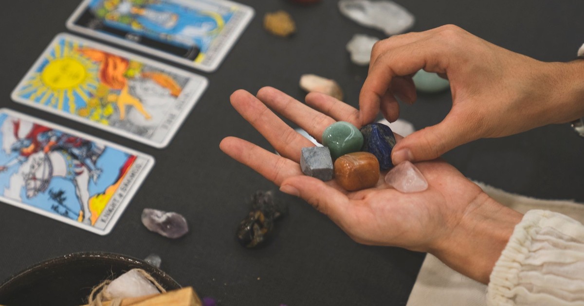 Person holding healing crystals with tarot cards in the background, symbolizing spirituality.