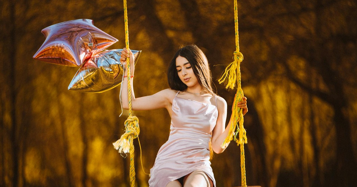 A serene scene of a woman in a pink dress sitting on a swing, holding star-shaped balloons.
