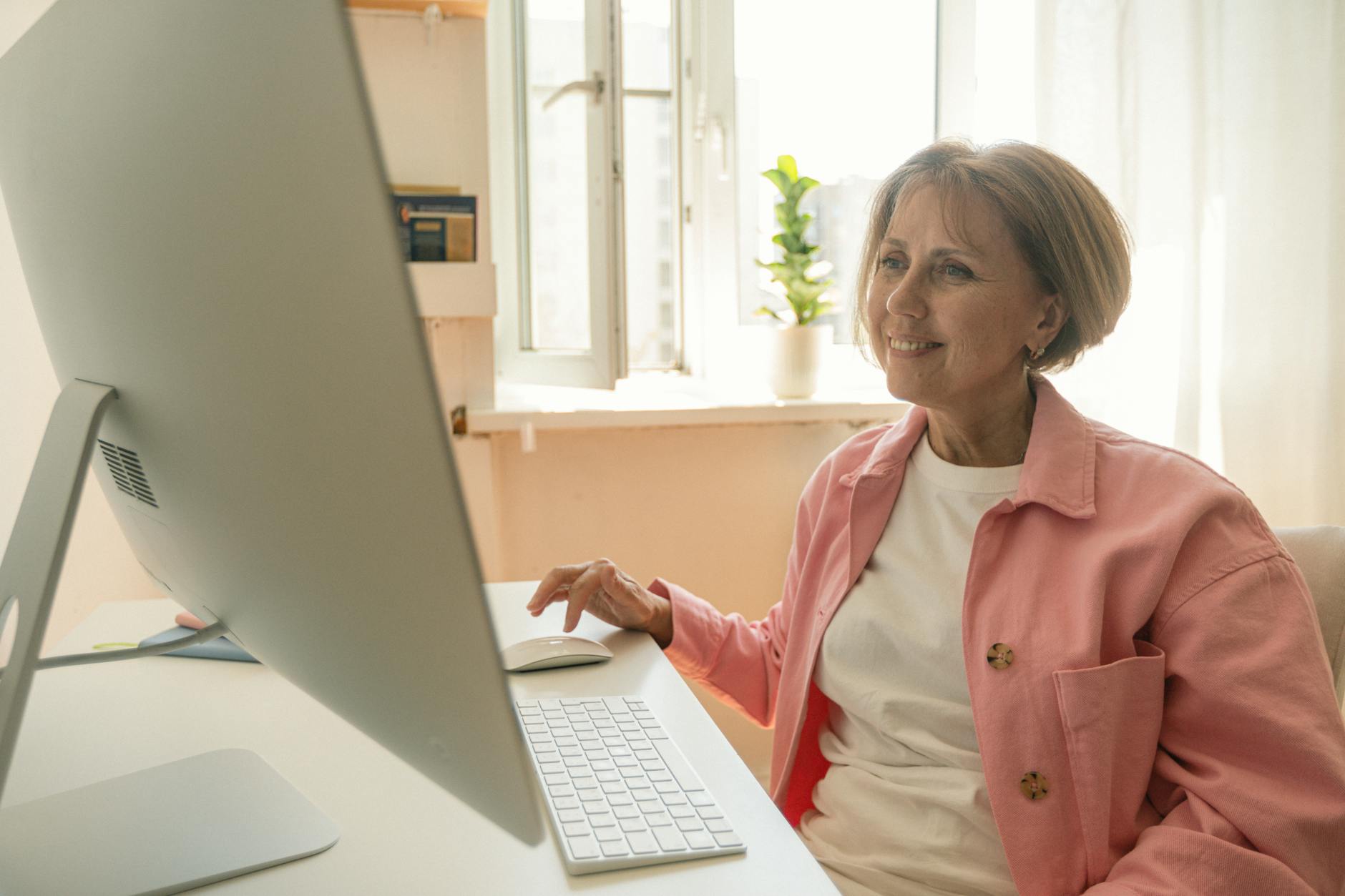 Smiling senior woman using a desktop computer at home, enjoying technology.