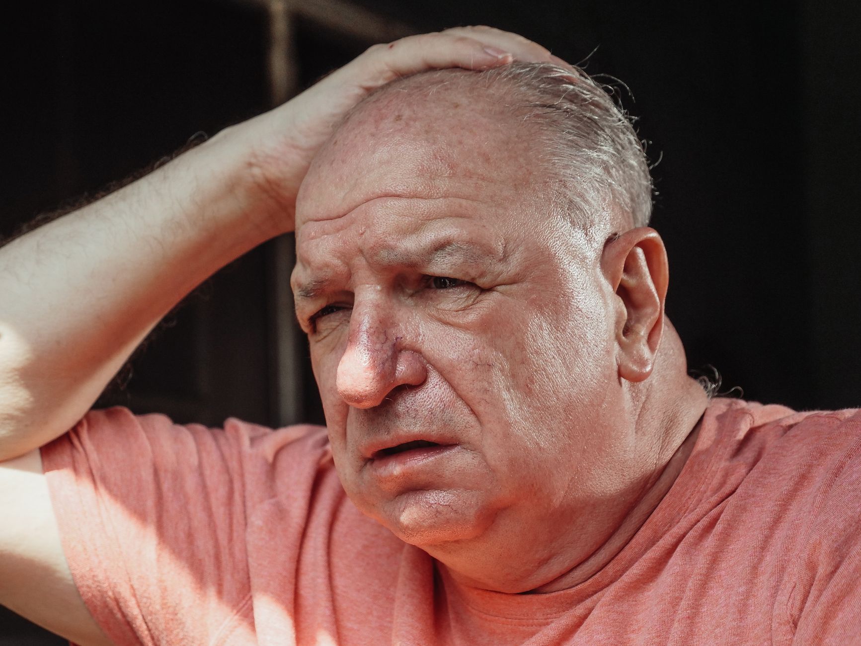 Close-up of a senior adult man looking troubled with hand on head, expressing stress.