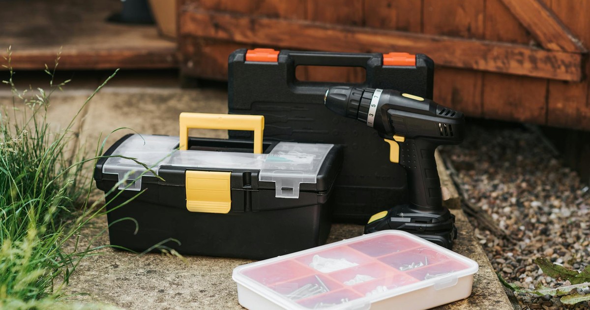 Electric screwdriver with black case placed near entrance of garage with boxes of instruments on sidewalk with grass on street