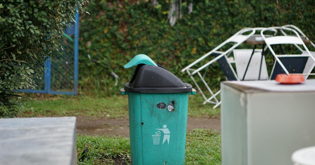 A green trash bin in a grassy outdoor area in Palembang, Indonesia.