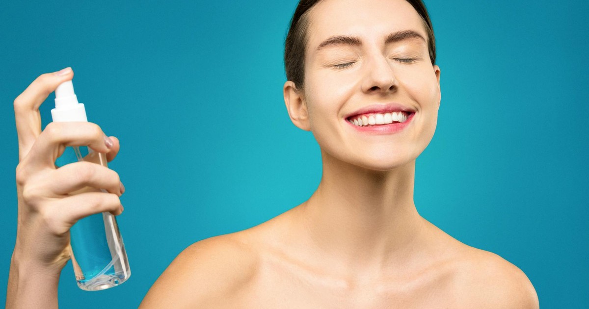 A happy woman with closed eyes sprays facial mist, emphasizing skincare and relaxation.