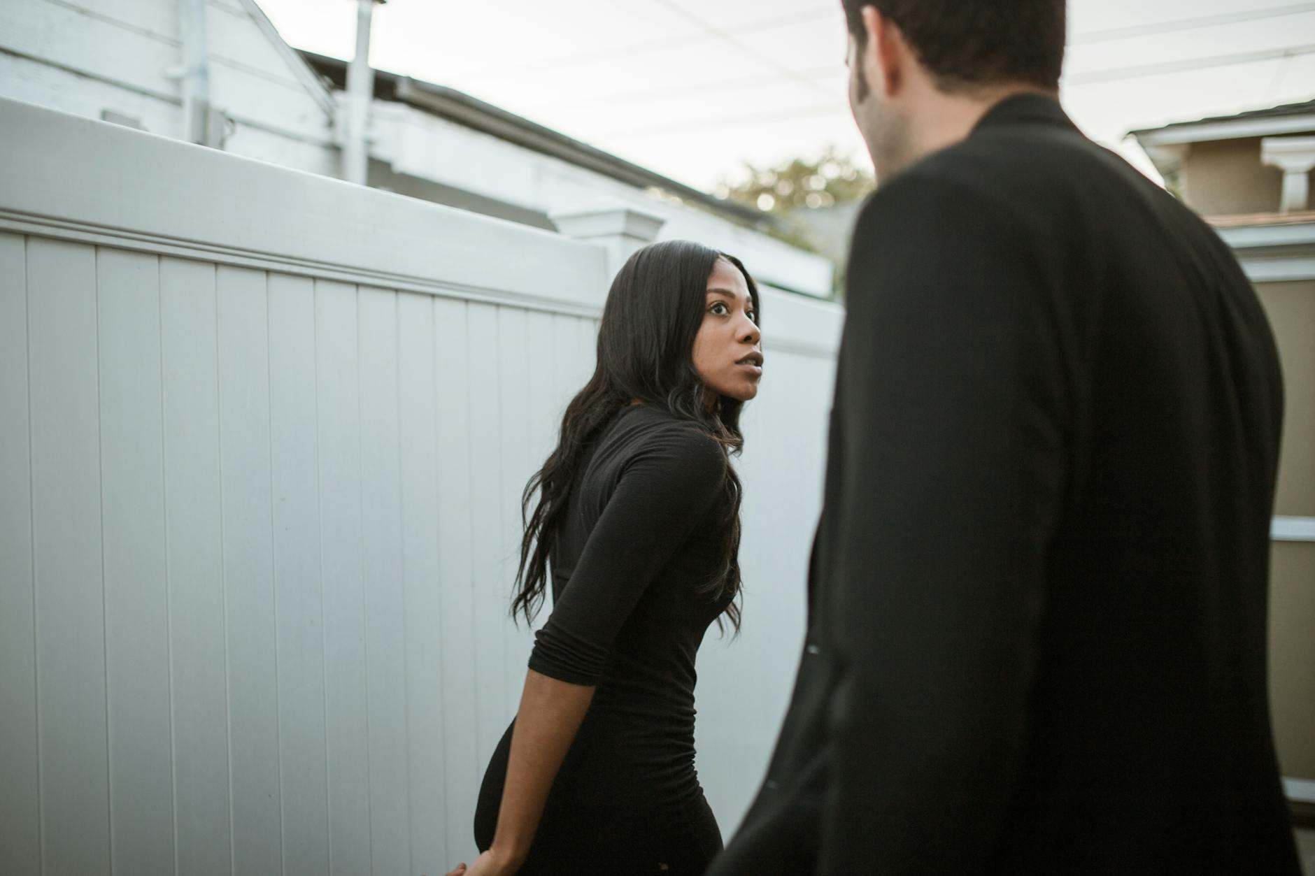 A black woman and a man in an intense conversation outside, displaying mixed emotions.